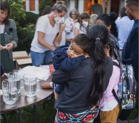  ?? RAY EWING/VINEYARD GAZETTE VIA AP ?? CAUGHT IN THE MIDDLE: A woman, who is part of a group of immigrants that had just arrived, holds a child as they are fed outside St. Andrew’s Episcopal Church, Wednesday, in Edgartown, on Martha’s Vineyard.