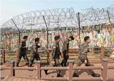  ?? [AP PHOTO] ?? South Korean army soldiers pass by a wire fence decorated with ribbons written with messages wishing for the reunificat­ion of the two Koreas at the Imjingak Pavilion in Paju, South Korea, near the border with North Korea on Friday. North and South...