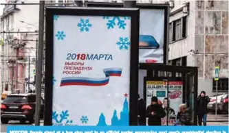  ??  ?? MOSCOW: People stand at a bus stop next to an official poster announcing next year’s presidenti­al election in Moscow yesterday. — AFP