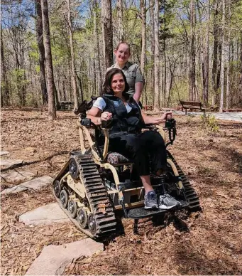  ?? Georgia Department of Natural Resources ?? Melanie Dunn, with the help of park ranger Leslie Mobley, demonstrat­es one of the all-terrain track chairs available in the state parks in Georgia.