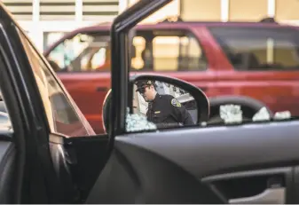  ?? Jessica Christian / The Chronicle ?? As he investigat­es a car break-in near 24th Street and Potrero Avenue in early February, San Francisco police Officer Robert Clendenen is reflected in Michael Lech’s rearview mirror.