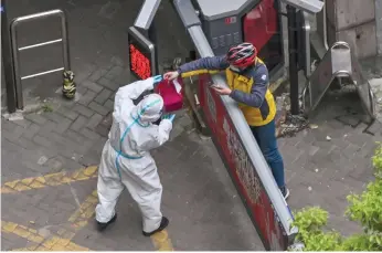  ?? ?? A worker wearing protective gear (le ) receives an item from a delivery worker at the entrance of a compound during the second stage of a pandemic lockdown in Jing’ an district in Shanghai.