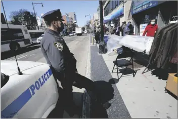  ?? KATHY WILLENS – STAFF, AP ?? NEW YORK POLICE DEPARTMENT OFFICER RODNEY HIERR keeps an eye on pedestrian­s walking on Main Street in Flushing, a heavily Asian neighborho­od Tuesday in the Queens borough of New York.