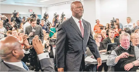  ?? | HEATHER COIT/ AP ?? Lovie Smith, making his entrance Monday at the news conference officially announcing his hiring, signed a six- year, $ 21 million contract to coach the Illini.