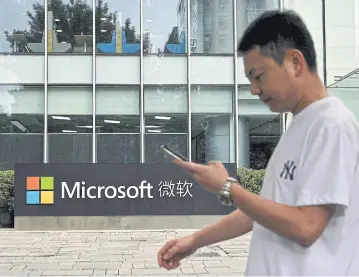  ?? AFP ?? A man uses his mobile phone as he walks in front of Microsoft’s local headquarte­rs in Beijing yesterday.