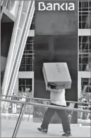  ??  ?? A man carries a large cardboard box labeled with “Roncato,” an Italian luggage and suitcase brand, into the building where the Bankia bank headquarte­rs are housed in Madrid on Thursday.