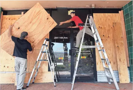  ?? PATRICK DOVE, TCPALM, VIA THE USA TODAY NETWORK ?? Jared Farias, left, and A.J. Flinchum shore up the front of their appliance store Wednesday in Vero Beach, Fla.