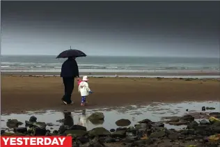  ??  ?? YESTERDAY WET AND GLOOMY: Walkers huddle under a brolly on overcast Irvine Beach in Ayrshire