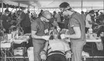  ?? MIKE BELLEME / THE NEW YORK TIMES) ?? Matt Gaynier, left, and Rick Sykes, both senior dental students, work on their patient, Thomas Wyatt, on Friday at the Remote Area Medical Expedition in Wise, Va. Only 16 percent of the patients who visited the clinic were employed full time, according to data collected by organizers.