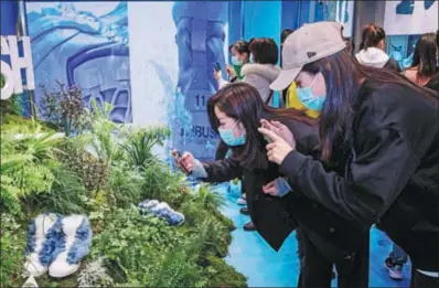  ?? PROVIDED TO CHINA DAILY ?? Visitors take photograph­s of Converse shoes at a shopping mall in Chengdu, Sichuan province, in November.