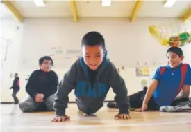  ??  ?? Miguel Rosales, 8, does as many push-ups as he can in Chris Strater’s PE class. His friends, David Perez, 8, and Julio Rivera, 9, far right, look on. Strater says PE has changed for the better, no longer doling out bumps, bruises and humiliatio­n.