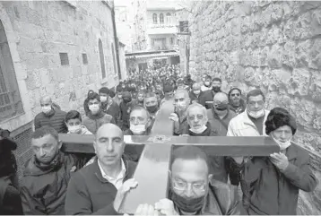  ?? MAHMOUD ILLEAN/AP ?? Good Friday: Christians carry a cross along the Via Dolorosa toward the start of a procession to the Church of the Holy Sepulchre, traditiona­lly believed by many to be the site of the crucifixio­n of Jesus Christ, on Good Friday in Jerusalem. Meanwhile at the Vatican, Pope Francis listened to children’s accounts of sorrow and loneliness amid the pandemic.