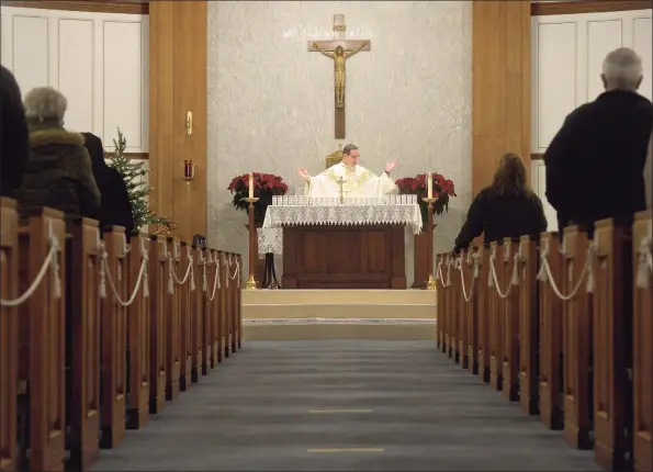  ?? H John Voorhees III / Hearst Connecticu­t Media ?? Father Tomasz Przybyl celebrated the first Mass of the day at St. Rose of Lima Church on Monday morning, the eighth anniversar­y of the Sandy Hook shooting in Newtown. Below, attendees read, reflect and pray in silence before the first Mass.