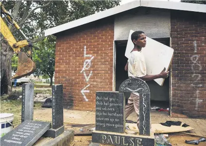  ?? Picture: Jacques Nelles ?? GRAVE CONCERN. A drug addict who was living in the empty office building in the cemetery removes his belongings as the bulldozer prepares to knock it down.