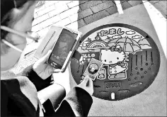  ??  ?? A visitor photograph­s a manhole cover featuring Hello Kitty in the Tama area of Tokyo, after getting a manhole card of the hatch. — Japan News-Yomiuri photo