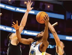  ?? D. Ross Cameron/Associated Press ?? The Warriors’ Andrew Wiggins shoots between Nets defenders Ben Simmons (left) and Nic Claxton. Wiggins, coming off an illness, could play on Monday.