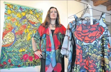  ?? SARA ERICSSON ?? Canning silk artist Holly Carr stands with a silk panel hanging behind her and a rack of clothing — including the wrap that she’s wearing — printed with her painted designs.