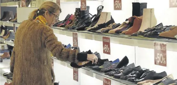  ??  ?? Una mujer mira zapatos en un pequeño establecim­iento, en época de rebajas.