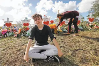  ?? Gerald Herbert / Associated Press ?? Chris Grady, a student at Marjory Stoneman Douglas High School, sits near a memorial outside the school for the 17 victims of Wednesday’s mass shooting in Parkland, Fla.