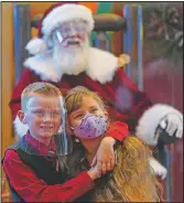  ?? (AP/Ashley Landis) ?? William Peargin (left) and Payton Peargin, both 8, pose for a socially distant photo with Santa Claus, who sits behind a sheet of plexiglass at Bass Pro Shop in Rancho Cucamonga, Calif.