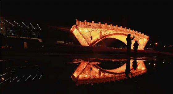  ?? —REUTERS ?? GOLDEN BRIDGE People take pictures in front of the “Golden Bridge on Silk Road” installati­on, set up outside the National Convention Center in Beijing ahead of the One Belt, One Road Forum, which opened on Sunday.