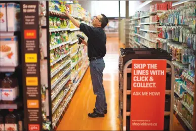  ?? Canadian Press photo ?? Grant Bone, Department Manager for Loblaw’s “Click and Collect” gathers a customer's order at one of the grocery chain’s outlets in Toronto on Thursday.