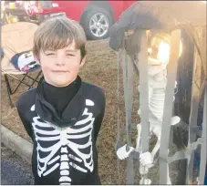  ?? Westside Eagle Observer/SUSAN HOLLAND ?? Young Rayce Ruiz, 7, of Gravette, dressed as a skeleton, poses beside another skeleton he encountere­d in a cage during the trunkor-treat event at the Gravette fall festival Saturday night. Rayce was one of many trick-or-treaters who enjoyed the activity at the festival. Many, both young and old, were dressed in costume.