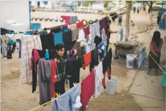  ??  ?? LEFT: A woman does laundry Thursday at Pan de Vida, where 290 people awaiting entry to the U.S. share 15 houses.