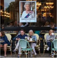  ?? AP PHOTO/EMILIO MORENATTI ?? People sit at a terrace bar Tuesday under a portrait of Queen Elizabeth II in central London.