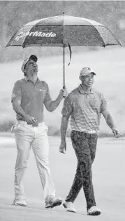  ?? Sam Greenwood / Getty Images ?? Jason Day, left, has umbrella duties on the sixth hole of a soggy practice round with Tiger Woods on Tuesday at the TPC Sawgrass.