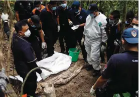  ?? — AFP, AP ?? A Malaysian police forensic team inspects a human body ( above) exhumed from an unmarked grave in Wang Burma, at the Malaysia- Thailand border outside Wang Kelian, on Tuesday. Rohingya migrants queue up for food at a temporary shelter in Bayeun, Aceh...