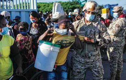  ?? Matias Delacroix / Associated Press ?? A woman, who is denied entry into the Dominican Republic, tries to put on her protective face mask as a soldier removes her from a line for not initially wearing the mask, at the border crossing in Dajabon, Dominican Republic, last month.