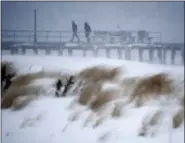  ?? ASSOCIATED PRESS ?? People walk on a small pier as snow covers the sand dunes during a snowstorm that hit the New Jersey Shore, Thursday in Ocean Grove, N.J. A massive winter storm swept from the Carolinas to Maine on Thursday, dumping snow along the coast and bringing...