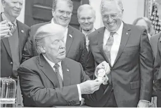  ?? Evan Vucci / Associated Press ?? President Donald Trump holds up a figurine handed to him by former Apollo 17 astronaut Jack Schmitt, right, on Monday in the Roosevelt Room of the White House.