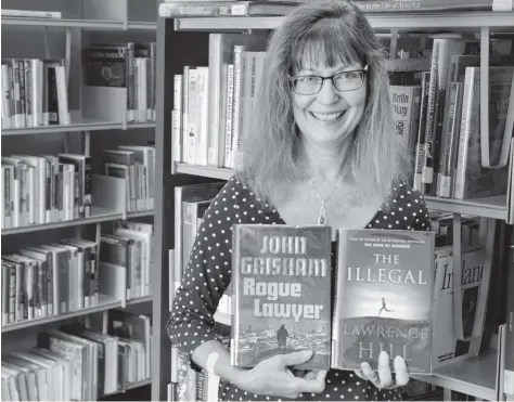  ?? [LIZ BEVAN / THE OBSERVER] ?? Sheryl Tilley, supervisor for the Woolwich and Wellesley library branches, holds up two of this summer’s hot reads at the Elmira Library. She says there have been more people checking out books this summer than she can remember in previous years.