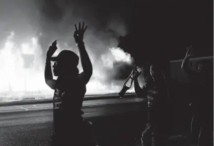  ?? [DAVID GOLDMAN/ASSOCIATED PRESS] ?? Protesters walk past police with their arms up as a building burns behind them in Kenosha, Wis., late Monday.