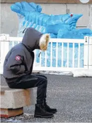  ?? THE ASSOCIATED PRESS ?? A person sits bundled against the cold near a blue lobster ice sculpture Thursdayco­utside the New England Aquarium in Boston.