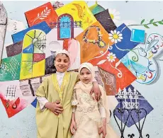  ??  ?? Children pose for a photo in front of a large graffiti depicting cultural elements including mosques, churches, old window lattices of the old town of Iraq’s northern city of Mosul, on the first night of the Muslim holy fasting month of Ramadan, during a celebratio­n hosted by a local cultural NGO.