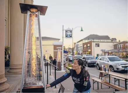  ?? MARK MIRKO/HARTFORD COURANT ?? Outdoor heaters are ignited outside the Main Street Mystic Bank and Bridge brew pub by staff member Samantha Lugo. The bustling, historic and low-lying downtown Mystic is an area environmen­talists say is threatened by the effects of climate change.