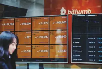  ?? Bloomberg ?? A pedestrian walks past monitors showing the prices of virtual currencies at the Bithumb exchange office in Seoul yesterday.