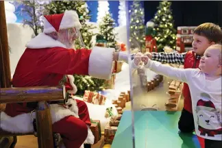  ?? SETH WENIG — THE ASSOCIATED PRESS ?? Julianna, 3, and Dylan, 5, Lasczak visit with Santa through a transparen­t barrier at a Bass Pro Shop in Bridgeport, Conn.. Santa Claus is coming to the mall — just don’t try to sit on his lap. Malls are doing all they can to keep the jolly old man safe from the coronaviru­s, including banning kids from sitting on his knee, no matter if they’ve been naughty or nice.