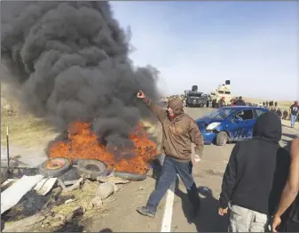  ?? AP PHOTO ?? Demonstrat­ors stand next to burning tires as armed soldiers and law enforcemen­t officers assemble to force Dakota Access pipeline protesters off private land where they had camped to block constructi­on.