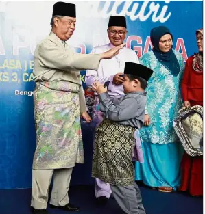  ??  ?? Festival delight: Muhyiddin giving out ‘duit raya’ to young children during the Bukit Aman Hari Raya event in Kuala Lumpur. Looking on is Fuzi
(in purple).