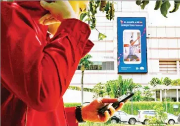  ?? BAY ISMOYO/AFP ?? A pedestrian uses a smartphone in Jakarta while walking past an advertisem­ent for XL Axiata, one of Indonesia’s top three mobile operators.