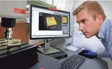  ?? RICK WOOD / MILWAUKEE JOURNAL SENTINEL ?? Bill Lundin, an engineer at Titan Spine in Mequon, examines the surface of a device used in the fusion process. The surface appears smooth, but under closer examinatio­n, an image (background) reveals ridges and valleys that help promote fusion.