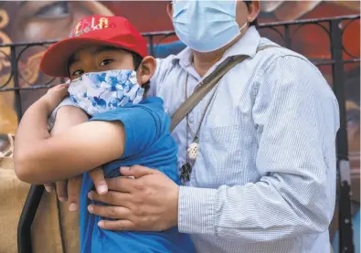  ?? Santiago Mejia / The Chronicle ?? Angel Pascual is embraced by his father Alejandro Pascual as they wait along 24th Street for Angel’s mother to come back from a store in San Francisco. Alejandro was laid off as a restaurant cook and his partner, Asuncion Morales, is also without work. Minorities are being disproport­ionately affected by the pandemic.