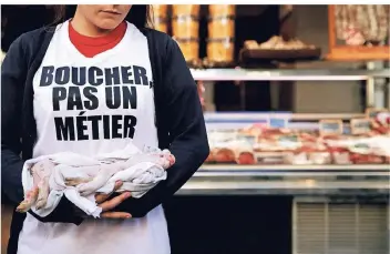  ?? FOTO: REUTERS ?? Ein Tierschutz-Aktivist der Gruppe „Boucherie Abolition“(Abschaffun­g der Fleischere­ien) hält vor einer Metzgerei in Paris ein totes Ferkel im Arm. Auf seinem Shirt steht „Metzger ist kein Beruf“.