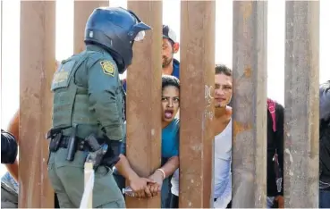  ?? AP PHOTO/GREGORY BULL ?? Migrants from Central America yell through a border wall at a U.S. Border Patrol agent after he pulled down a banner Sunday in San Diego. Migrants approachin­g the U.S. border from Mexico were enveloped with tear gas Sunday after a few tried to breach the fence separating the two countries.