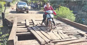  ??  ?? Una motociclis­ta maniobra para cruzar sobre el obsoleto y peligroso puente de madera.