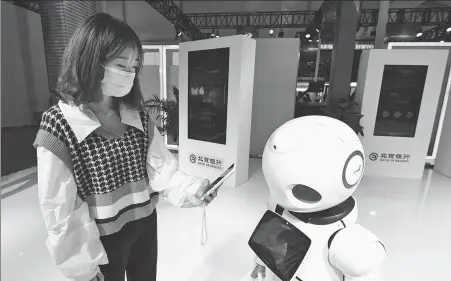  ?? REN CHAO / XINHUA ?? A visitor interacts with a smart robot during an expo promoting financial inclusion in Beijing.